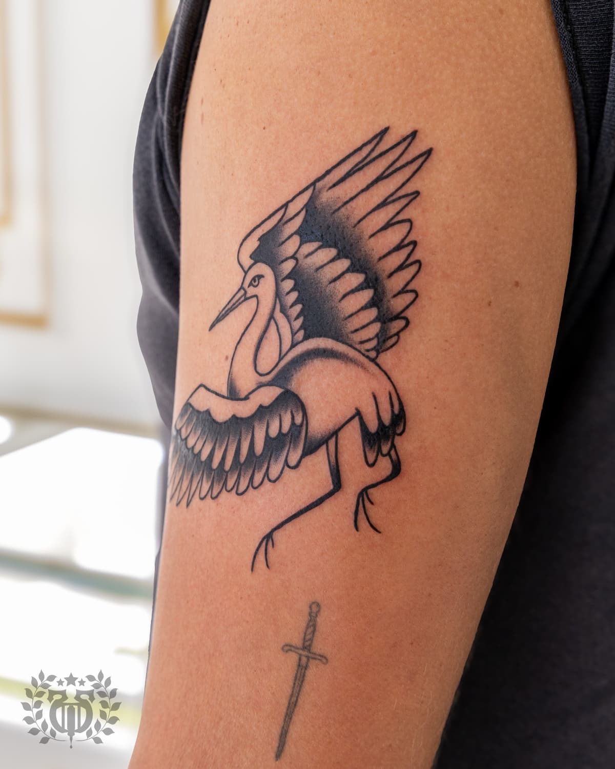 Blackwork tattoo crane with spread wings on upper arm in Los Angeles