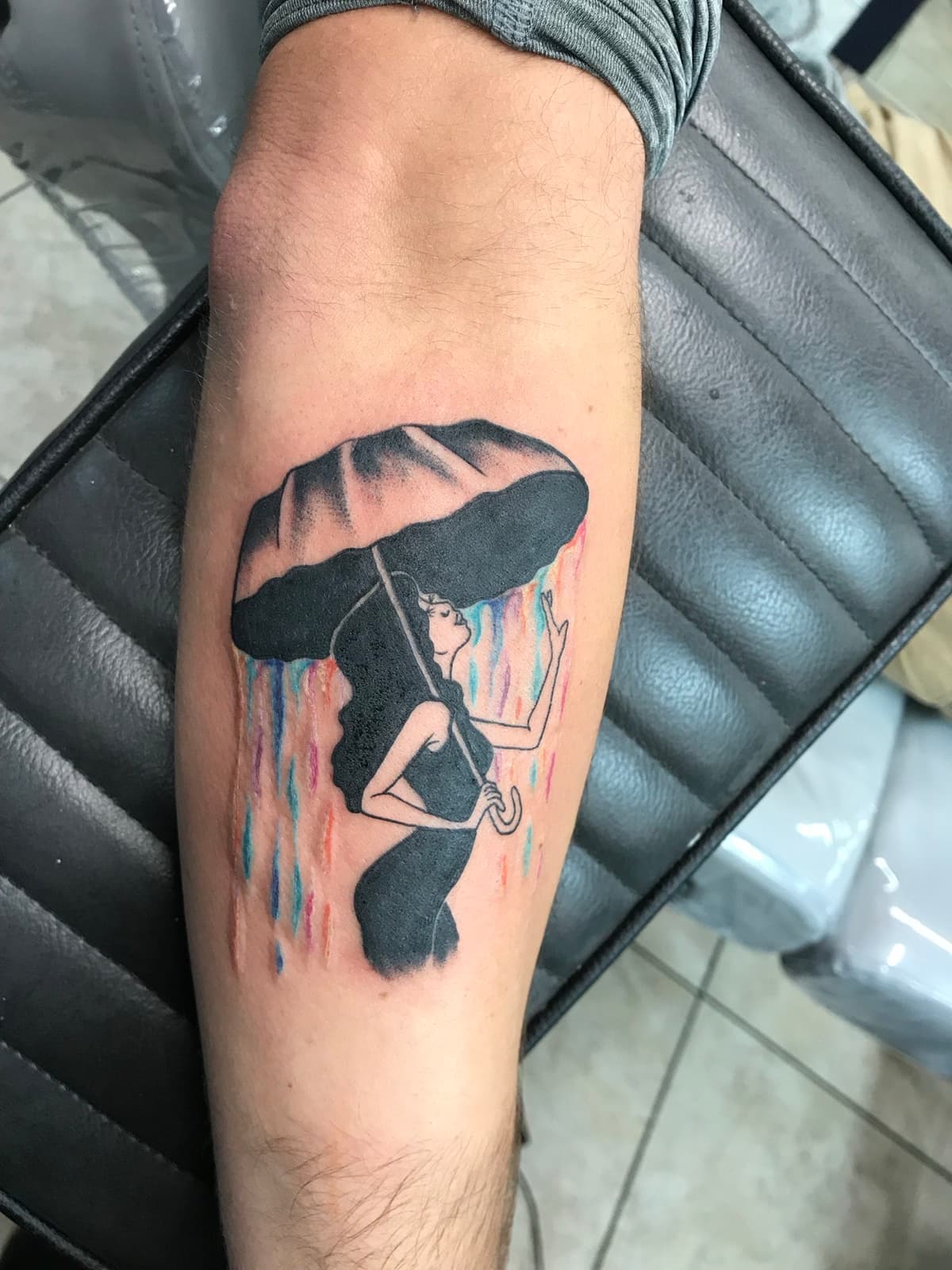 Blackwork tattoo silhouette woman reading with colorful sky on forearm in Los Angeles