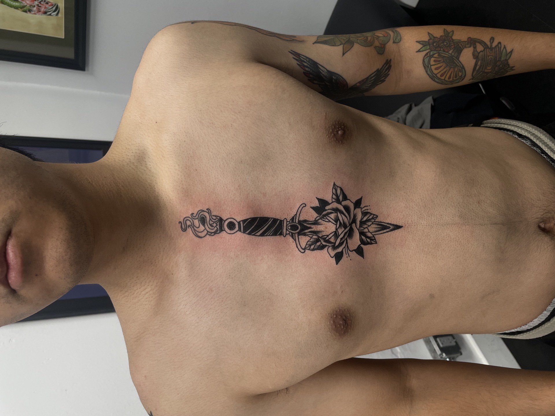 Blackwork tattoo dagger with snake and rose on sternum chest in Los Angeles