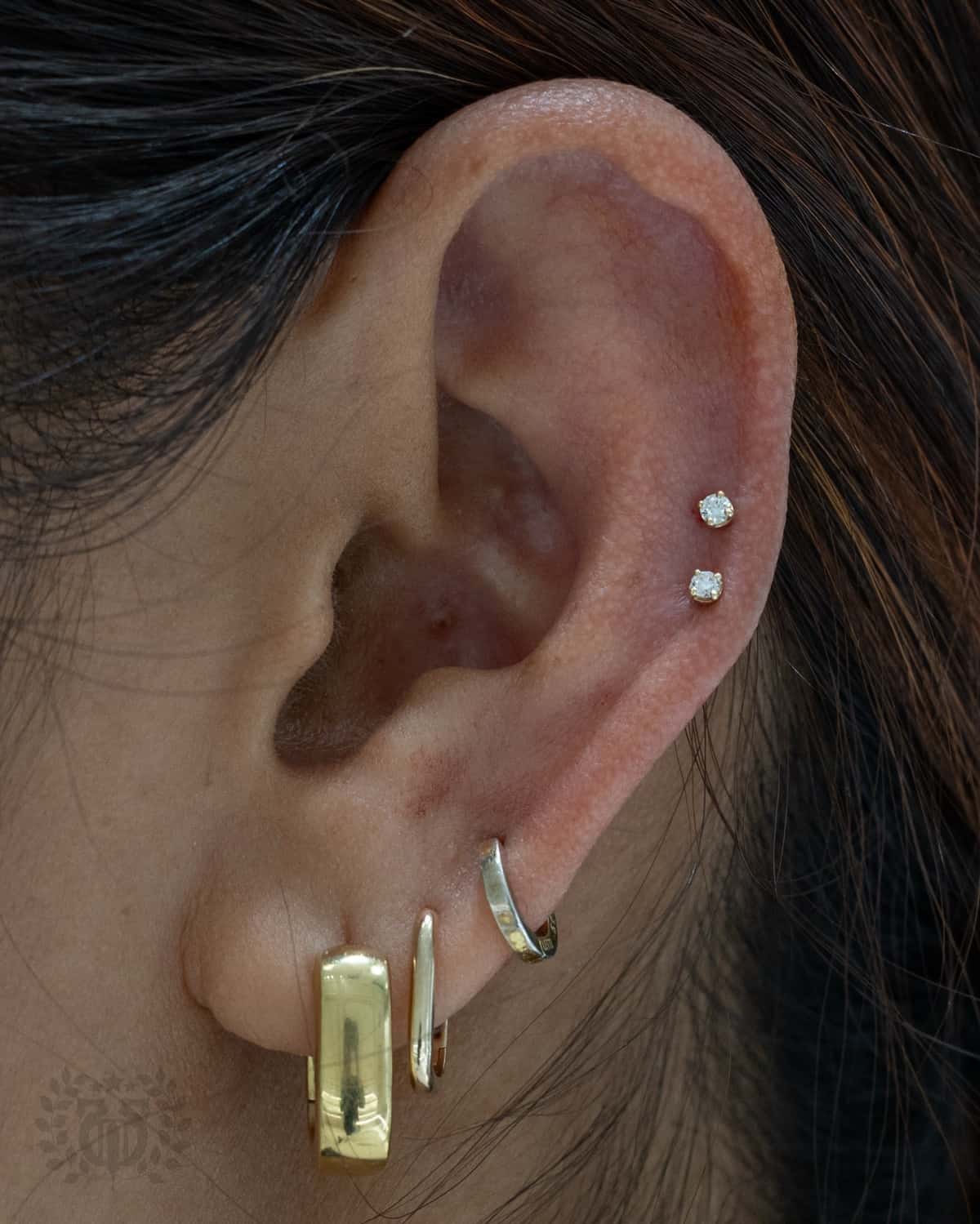 Mid-ear double CZ snakebite cartilage studs with gold lobe earrings at Apollo Studio Los Angeles